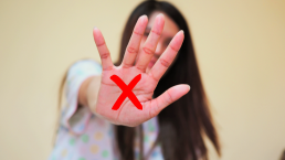 Mulher com a mão estendida e um X vermelho desenhado nela representando denúncia contra violência.